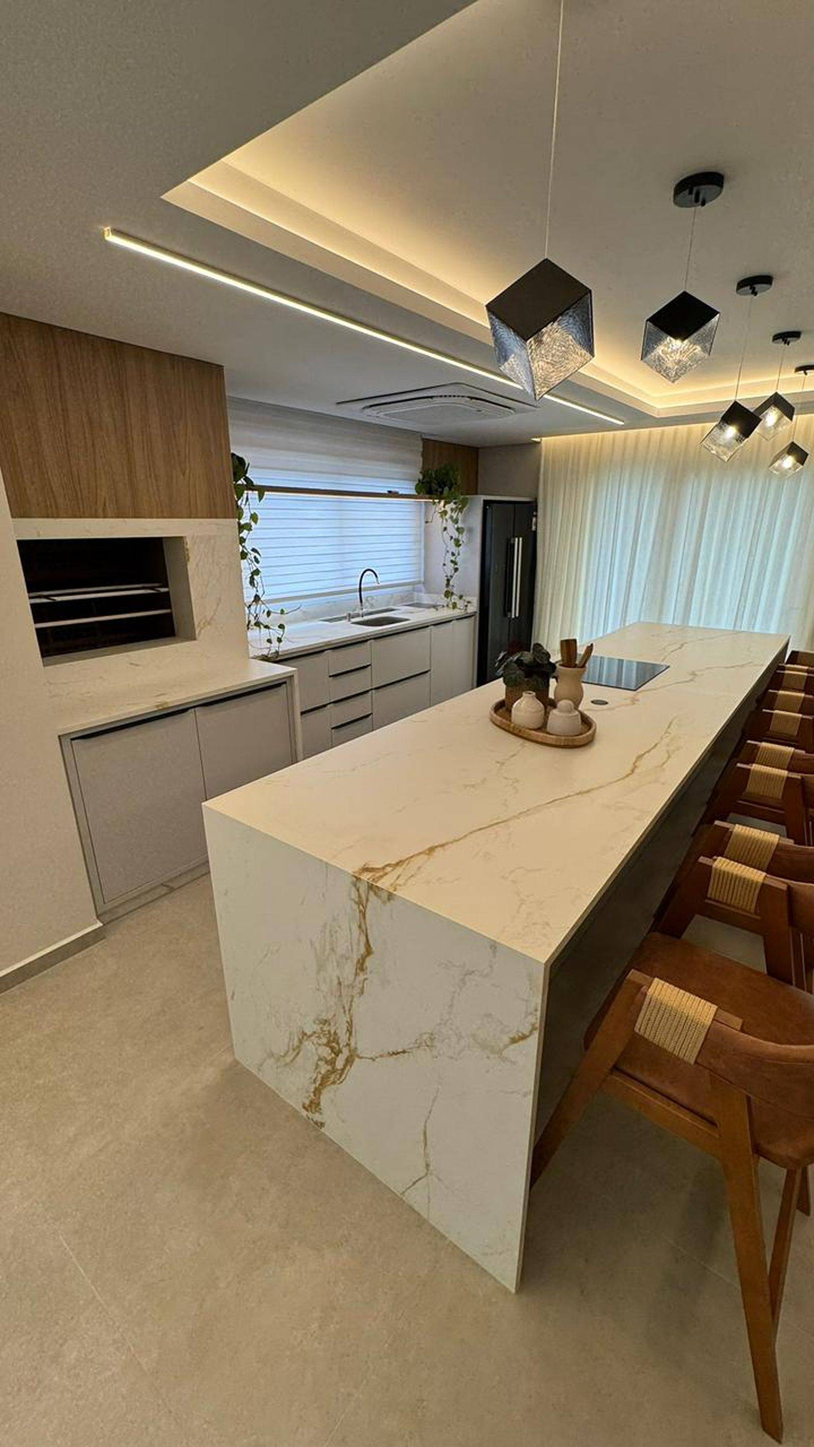 Espaço gourmet completo com ilha em pedra, bancada de apoio e painel em lâmina ultracompacta.